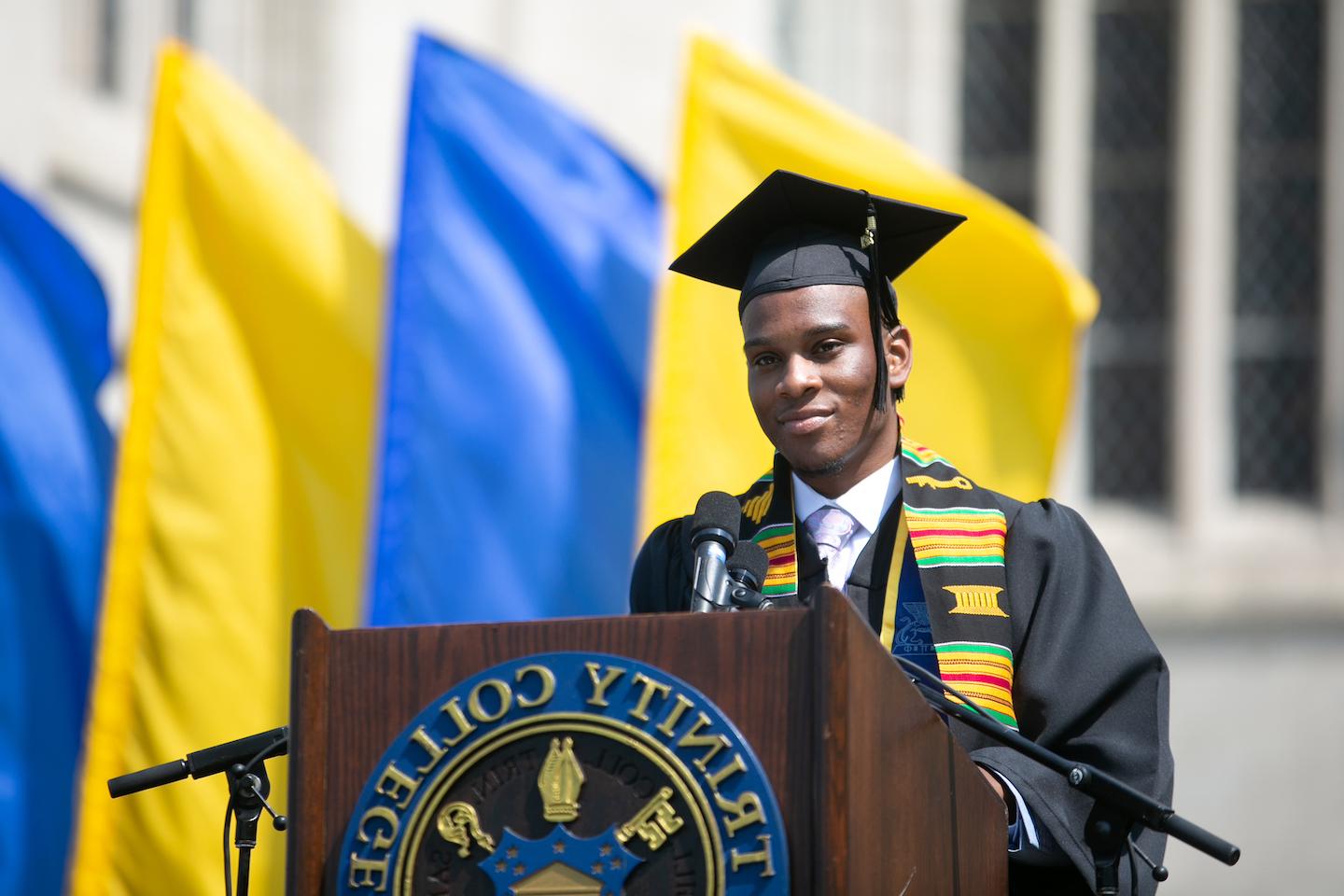 A trinity college grad standing at the graduation podium ready to speak